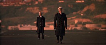 Movie still from “Behind Enemy Lines” (2001), directed by John Moore – Two men in military uniforms walking across a runway; Wide shot, Low angle