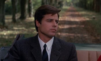 Movie still from “Belle de Jour” (1967), directed by Luis Buñuel – A man wearing a suit and tie sitting in a park; Close Up shot, Over the shoulder angle