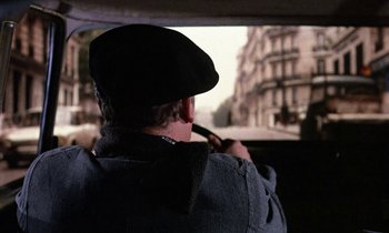 Movie still from “Belle de Jour” (1967), directed by Luis Buñuel – A man driving a car on a street; Medium shot, Over the shoulder angle