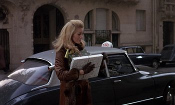 Movie still from “Belle de Jour” (1967), directed by Luis Buñuel – A woman walking down the street holding a suitcase; Medium shot, Over the shoulder angle