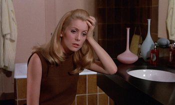 Movie still from “Belle de Jour” (1967), directed by Luis Buñuel – A woman sitting at a counter in a bathroom; Close Up shot, High angle
