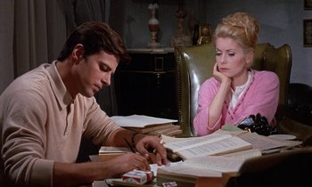 Movie still from “Belle de Jour” (1967), directed by Luis Buñuel – A man and a woman sitting at a table with papers; Medium shot, High angle
