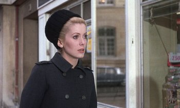 Movie still from “Belle de Jour” (1967), directed by Luis Buñuel – A woman wearing a black coat and a black hat; Close Up shot, Over the shoulder angle