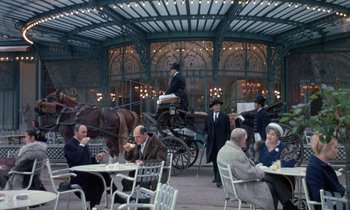 Movie still from “Belle de Jour” (1967), directed by Luis Buñuel – A group of people sitting at tables with horse and carriages; Wide shot, High angle