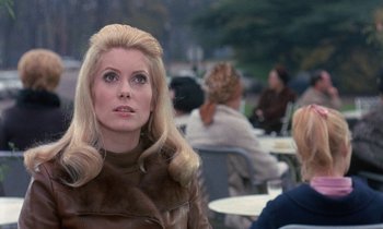 Movie still from “Belle de Jour” (1967), directed by Luis Buñuel – A woman with blonde hair sitting at a table with other people; Close Up shot, Over the shoulder angle