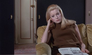 Movie still from “Belle de Jour” (1967), directed by Luis Buñuel – A woman sitting in a chair holding her head with one hand; Medium shot, High angle