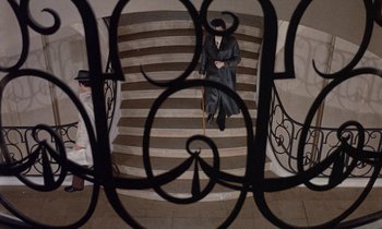 Movie still from “Belle de Jour” (1967), directed by Luis Buñuel – A man sitting on top of a set of stairs; Wide shot, Overhead angle