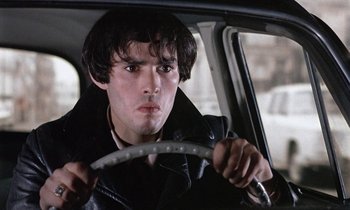 Movie still from “Belle de Jour” (1967), directed by Luis Buñuel – A young man driving a car in the rain; Close Up shot, Low angle