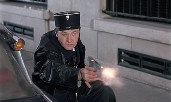 Movie still from “Belle de Jour” (1967), directed by Luis Buñuel – A man wearing a uniform and a hat is holding a gun; Medium shot, Low angle