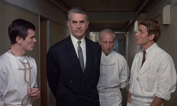 Movie still from “Belle de Jour” (1967), directed by Luis Buñuel – A group of men standing next to each other in a hallway; Medium shot, Low angle