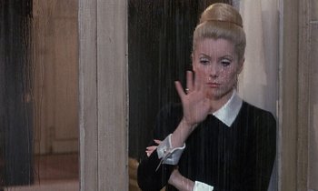 Movie still from “Belle de Jour” (1967), directed by Luis Buñuel – A woman in black and white shirt making a hand gesture; Medium shot, Over the shoulder angle