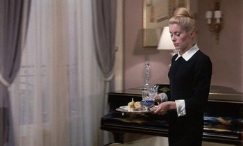 Movie still from “Belle de Jour” (1967), directed by Luis Buñuel – A woman holding a tray of food in front of a piano; Medium shot, Low angle