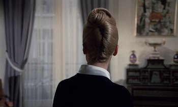 Movie still from “Belle de Jour” (1967), directed by Luis Buñuel – A woman with a bun in a room; Close Up shot, Over the shoulder angle