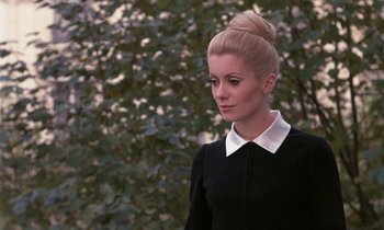 Movie still from “Belle de Jour” (1967), directed by Luis Buñuel – A woman in a black dress with a white collar and a bun; Close Up shot, Over the shoulder angle