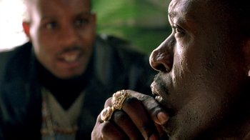A man is eating something while another man looks on