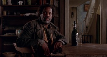 Movie still from “Beloved” (1998), directed by Jonathan Demme – A man sitting at a table with a bottle of wine; Medium shot, Low angle