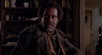 Movie still from “Beloved” (1998), directed by Jonathan Demme – An older man in a brown jacket sitting in front of a bookshelf; Close Up shot, Low angle