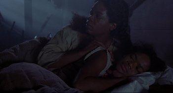 Movie still from “Beloved” (1998), directed by Jonathan Demme – A woman laying in a bed with another woman in her arms; Medium shot, High angle