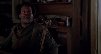 Movie still from “Beloved” (1998), directed by Jonathan Demme – A man standing in front of a shelf in a room; Medium shot, Low angle
