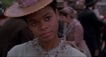 Movie still from “Beloved” (1998), directed by Jonathan Demme – A young girl wearing a hat and a necklace; Close Up shot, Over the shoulder angle