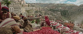 Movie still from “Ben-Hur” (2016), directed by Timur Bekmambetov – A group of people sitting on a bench near a bunch of red peppers; Extreme Wide shot, High angle