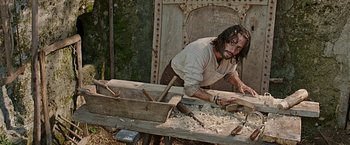 Movie still from “Ben-Hur” (2016), directed by Timur Bekmambetov – A man working with wood on a wooden bench; Medium shot, High angle