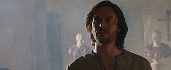 Movie still from “Ben-Hur” (2016), directed by Timur Bekmambetov – A man with long hair and a beard standing next to a statue; Close Up shot, Over the shoulder angle