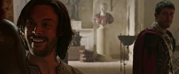 Movie still from “Ben-Hur” (2016), directed by Timur Bekmambetov – A man with long brown hair standing next to a statue; Close Up shot, Over the shoulder angle
