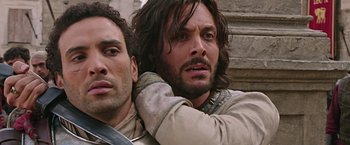 Movie still from “Ben-Hur” (2016), directed by Timur Bekmambetov – A man with long hair is holding another man's shoulder; Close Up shot, Low angle