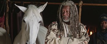 Movie still from “Ben-Hur” (2016), directed by Timur Bekmambetov – An older man with dreadlocks is sitting next to a white horse; Close Up shot, Over the shoulder angle