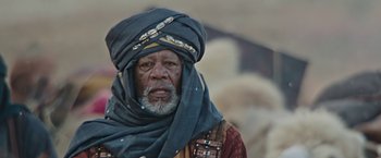 Movie still from “Ben-Hur” (2016), directed by Timur Bekmambetov – An older man wearing a blue turban and a red shirt; Close Up shot, Over the shoulder angle