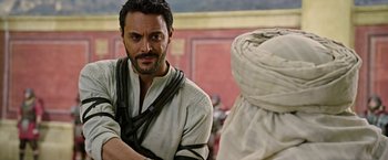Movie still from “Ben-Hur” (2016), directed by Timur Bekmambetov – A man with a beard and mustache wearing a white shirt; Medium shot, Over the shoulder angle