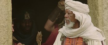 Movie still from “Ben-Hur” (2016), directed by Timur Bekmambetov – An older man in a white turban is holding a wooden stick; Medium shot, Over the shoulder angle