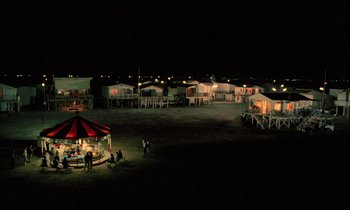 Movie still from “Betty Blue” (1986), directed by Jean-Jacques Beineix – A group of people standing around a gazebo at night; Extreme Wide shot, High angle