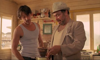 Movie still from “Betty Blue” (1986), directed by Jean-Jacques Beineix – A man in a hat and a man in a white shirt and a man in a tan jacket and a man in a white shirt and a man; Medium shot, Low angle