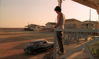 Movie still from “Betty Blue” (1986), directed by Jean-Jacques Beineix – A man standing next to an old car on a porch; Wide shot, Low angle