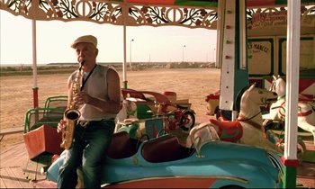 Movie still from “Betty Blue” (1986), directed by Jean-Jacques Beineix – A man playing a saxophone on a carousel; Wide shot, Low angle