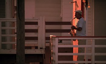 Movie still from “Betty Blue” (1986), directed by Jean-Jacques Beineix – A man playing a saxophone on a porch; Wide shot, Low angle