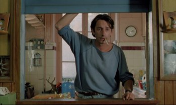 Movie still from “Betty Blue” (1986), directed by Jean-Jacques Beineix – A man standing at a counter in front of a window; Medium shot, Low angle