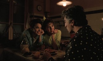 Movie still from “Betty Blue” (1986), directed by Jean-Jacques Beineix – A group of people sitting around a table; Medium shot, Over the shoulder angle