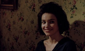 Movie still from “Betty Blue” (1986), directed by Jean-Jacques Beineix – A young woman smiling for the camera in front of a floral wallpaper; Close Up shot, Over the shoulder angle