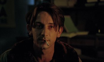Movie still from “Betty Blue” (1986), directed by Jean-Jacques Beineix – A young man smoking a cigarette while sitting in a room; Close Up shot, Over the shoulder angle