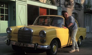 Movie still from “Betty Blue” (1986), directed by Jean-Jacques Beineix – A man leaning on the hood of an old yellow car; Wide shot, Low angle