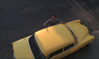 Movie still from “Betty Blue” (1986), directed by Jean-Jacques Beineix – A man standing on the hood of a yellow car; Wide shot, Overhead angle