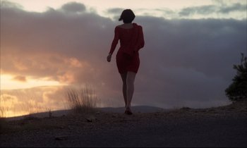 Movie still from “Betty Blue” (1986), directed by Jean-Jacques Beineix – A woman in a red dress walking on a dirt road; Extreme Wide shot, Low angle