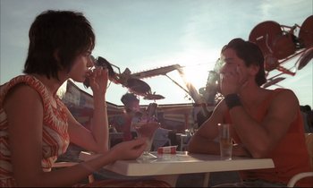 Movie still from “Betty Blue” (1986), directed by Jean-Jacques Beineix – A group of people sitting at a table with drinks; Medium shot, Low angle