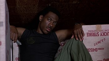 Movie still from “Beverly Hills Cop” (1984), directed by Martin Brest – A man sitting on the ground with his hands on his knees; Close Up shot, High angle