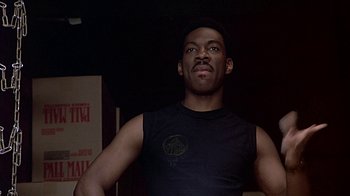 Movie still from “Beverly Hills Cop” (1984), directed by Martin Brest – A man standing in a room wearing a black shirt; Close Up shot, Low angle