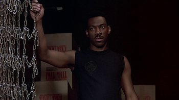 Movie still from “Beverly Hills Cop” (1984), directed by Martin Brest – A man in a black tank top holding a knife; Medium shot, Low angle