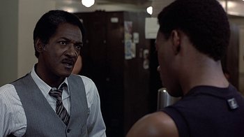Movie still from “Beverly Hills Cop” (1984), directed by Martin Brest – A man in a suit and tie talking to another man in a suit and tie in front of a mirror; Close Up shot, Over the shoulder angle